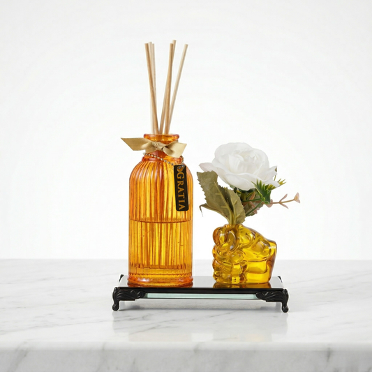 Orange diffuser bottle with reeds placed alongside a human fist shaped flower vase with a golden glass base