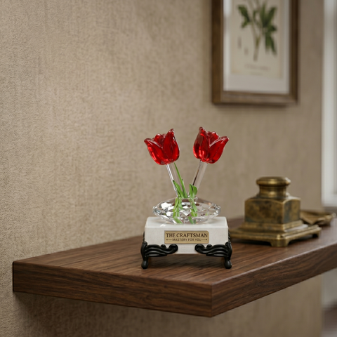 Decorative crystal red tulips placed on a white marble base on a wooden shelf with a neutral wall background.