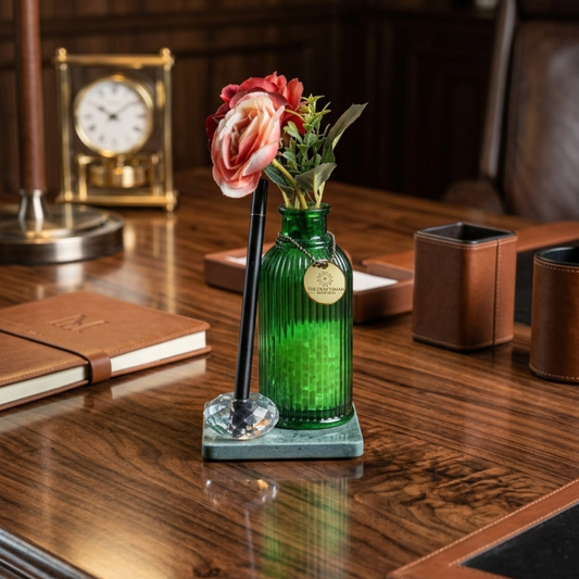 Green glass vase filled with fragrance beads with flowers placed on a green marble with crystal pen stand