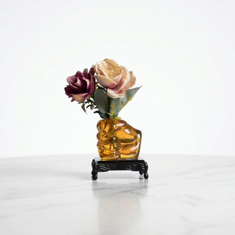 Glass human fist shaped flower vase paperweight placed on black glass base with traditional foots