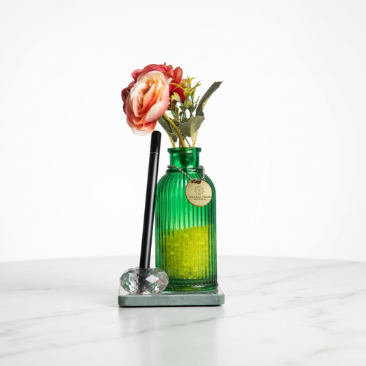 Green glass vase filled with fragrance beads with flowers placed on a green marble with crystal pen stand