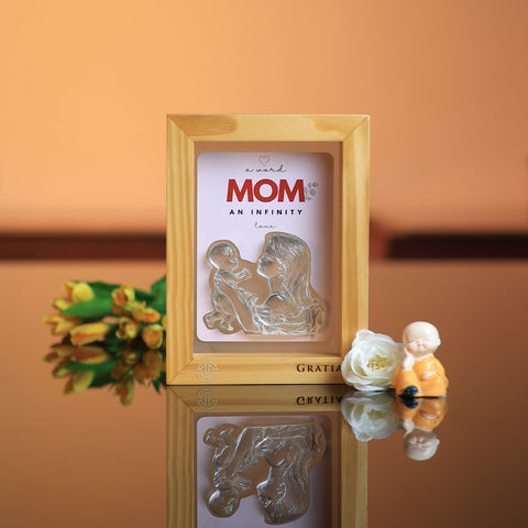 Decorative plaque with 'MOM' and a mother-child illustration on a reflective surface with a blurred background.