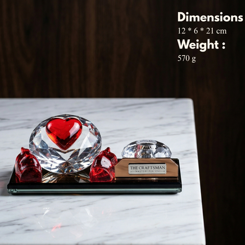 Crystal glass pen stand with red hands protecting a heart on diamond with crystal pen stand on a golden glass base.