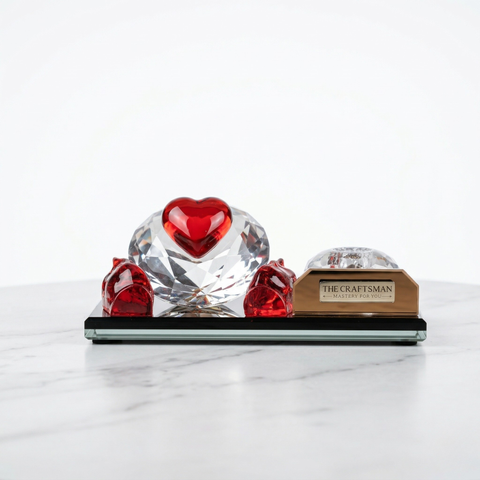 Crystal glass pen stand with red hands protecting a heart on diamond with crystal pen stand on a golden glass base.