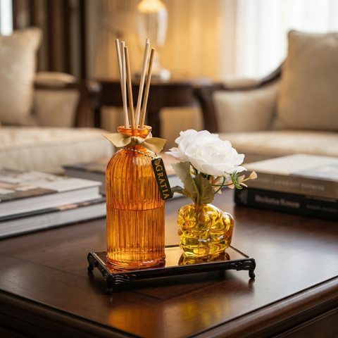Orange diffuser bottle with reeds placed alongside a human fist shaped flower vase with a golden glass base 